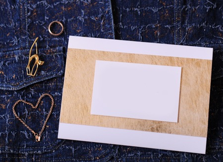Gold jewelry and certificate with empty blank for design on a blue denim background. Ring, brooch in the form of cat, bracelet chain lies like heart.の写真素材