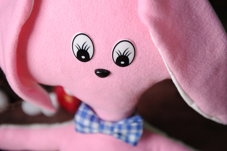 Big cute pink toy soft rabbit in blue plaid bow tie, close-up. Easter decor in the backgroundの写真素材