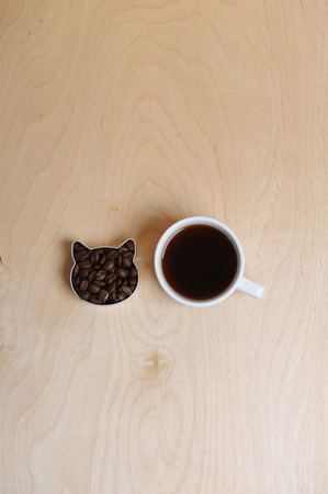 Cat head of coffee beans and cup of coffee. On light woody background, top viewの写真素材