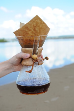 Alternative coffee brewing in hand on background of the sky and sandy beachの写真素材
