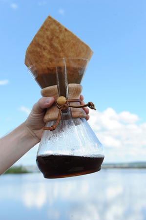 Alternative coffee brewing in hand on background of the sky and waterの写真素材