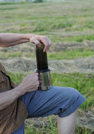 A young man is preparing coffee in open air. Alternative brewing of coffee in travel. Summer landscape in the fieldの写真素材