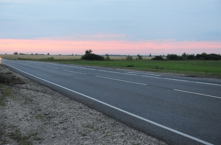 Pink sunset on empty road with markings. Country landscape. Atmosphere of travelの写真素材