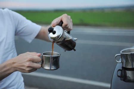 Alternative brewing coffee in a french press on the hood of a car on the side of the road on journeyの写真素材