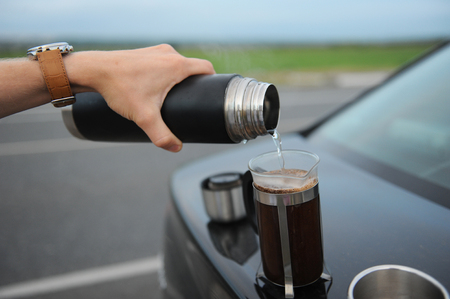 Alternative brewing coffee in a french press on the hood of a car on the side of the road on journeyの写真素材