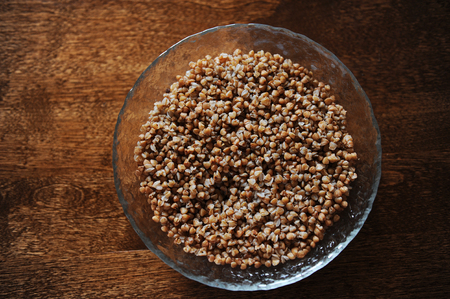 Large glass bowl of boiled buckwheat on a brown wooden texture tableの写真素材