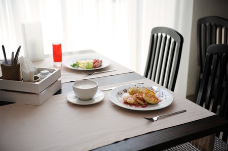Two different breakfasts are served in restornae. Cheesecakes and eggs with sausages, coffeeの写真素材