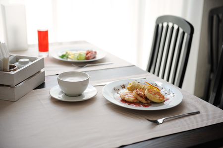 Two different breakfasts are served in restornae. Cheesecakes and eggs with sausages, coffeeの写真素材
