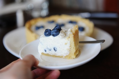 Piece of cheesecake with blueberries on white plate in hand in focus on the background of whole...