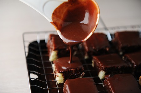 Dessert lamington is poured over chocolate icing on baking tray with grill. Cooking processの写真素材
