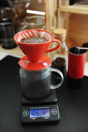 Coffee brewing process. Red ceramic dripper on electronic scale. Blooming. Manual grinder. Specialty concept. Paper filterの写真素材
