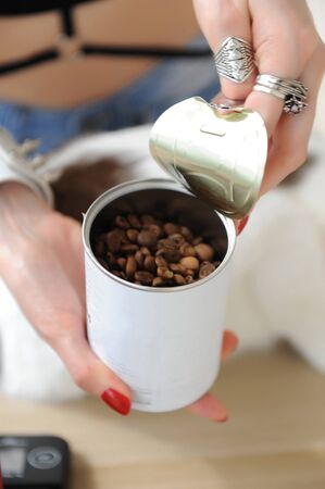 Barista girl opens tin can with coffee close up. Freshly roasted. Red manual grinder. White catの写真素材