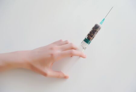 Coffee beans in a medical syringe in the hand. Caffeine addiction symbol. Medical and healthcare conceptの写真素材
