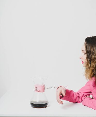 Beautiful girl in pink jacket is fastened with cuffs to coffee jug. Metaphor of passion, affection, caffeine addiction.の写真素材