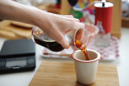 Manual coffee brewing still life. Pouring filter coffee from glass jug into cup. Bamboo tray. Third...
