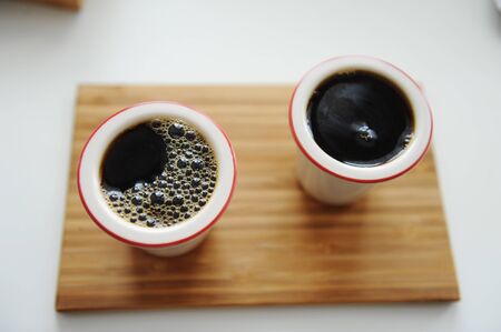 Fresh black filter coffee in two ceramic cups without handle on bamboo tray. White background. Top view, close up. Third wave specialty aestheticsの写真素材