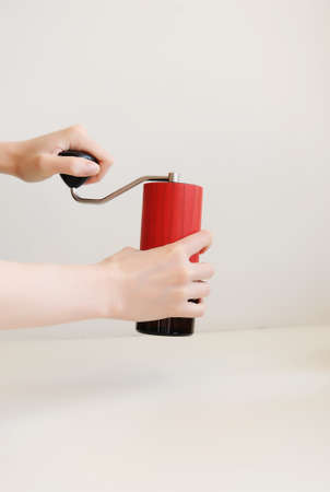Red manual coffee grinder in the hands on white backround