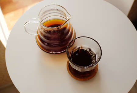 Black filter coffee served in a jug and a glass on a white round table. Top view. Specialty third wave conceptの写真素材