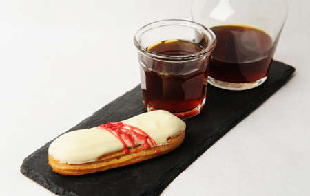 Freshly brewed black coffee served in glass carafe on slate board with french dessert eclair. White...