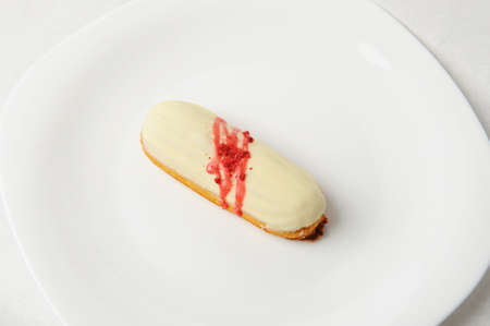 Yummy french dessert eclair with vanilla cream and strawberry sauce on white plate. Elegant serving...