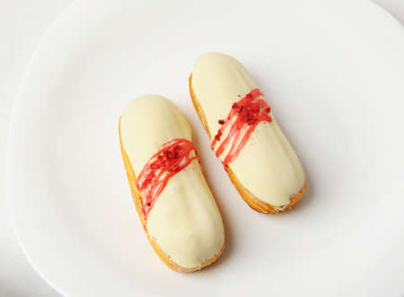 Yummy french dessert eclair with vanilla cream and strawberry sauce on white plate. Elegant serving...