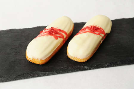 Yummy french dessert eclair with vanilla cream and strawberry sauce served on white plate. Elegant...