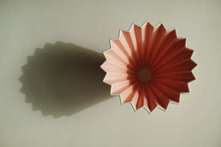 Pink origami coffee dripper on white background. Bright sunlight and distinct geometric shadowの写真素材