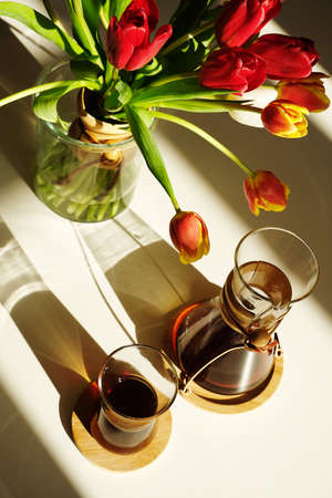 Specialty coffee aesthetics still life. Freshly brewed black coffee in glass decanter. Flower bouquet composition decorated in coffee style in sunlightの写真素材