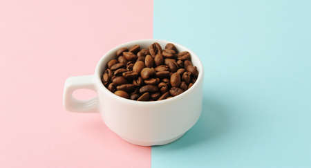 Coffee beans in white cup on geometric two-tone pink and blue backgroundの写真素材