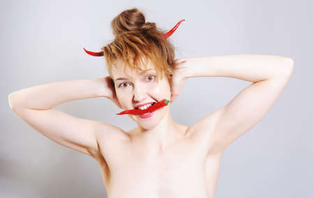 Funny girl portrait as a devil with the red chili peppers horns, holding another pod of pepper in the teethの写真素材