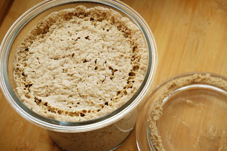 Homemade rye leaven sourdough in open glass jar top view on wooden tableの写真素材