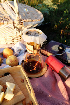 Summer picnic setting in the meadow in the rays of the sunset. Wicker basket, baguette, cheese,...