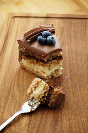 Piece of Kiev cake with chocolate icing and blueberries. A bite of cake on a fork