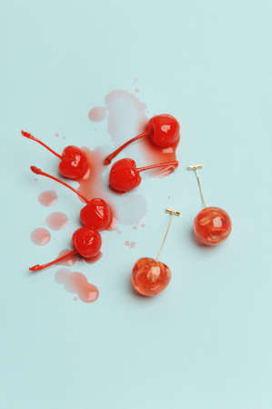 Charming earrings in the shape of cherries with dried flowers and natural cocktail cherries with spilled syrup on light blue background. Jewelry advertising conceptの写真素材