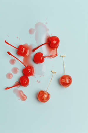 Charming earrings in the shape of cherries with dried flowers and natural cocktail cherries with spilled syrup on light blue background. Jewelry advertising conceptの写真素材
