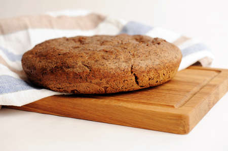 Fresh homemade round malted rye bread on wooden board, linen fabric. On white background