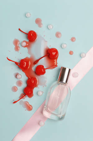 A bottle of perfume on light blue background with pink ribbon. Cocktail cherries in spilled syrup....