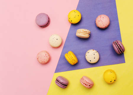 French dessert colorful macarons on a three-tone pink, yellow and violet geometric background, top viewの写真素材