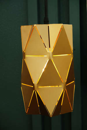 Gold-colored metal pendant lamp on green wall background, lampshade close-up. interior detailsの写真素材