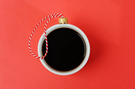 White cup of black espresso coffee decorated as Christmas ball on a red and white ribbon. Close-up, red background. new year holiday conceptの写真素材