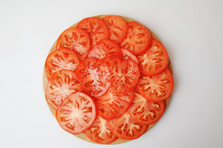 Fresh tomato slices are laid out on a round board. White background, top view.の写真素材