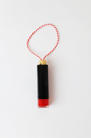 Lipstick as a Christmas tree toy on a red-white string on a white background. Beauty cosmetic New...