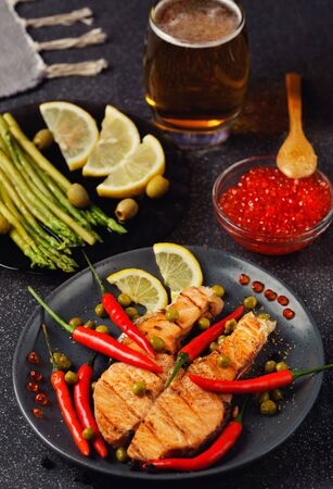 Beautiful still life. Salmon steak, chili pepper, red caviar, asparagus, a glass of beer on a dark backgroundの写真素材
