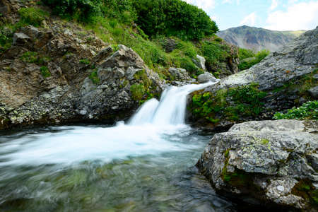 landscape. mountain river flows between large stones against the backdrop of green hillsの写真素材