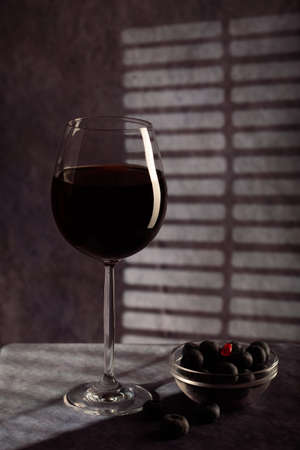 still life. beautiful glass with red wine, plate with blue berries on a dark background with creative lightingの写真素材