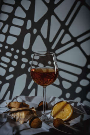 Still life. Big beautiful glass, sea clam shell, lemon on a dark background with creative lightingの写真素材