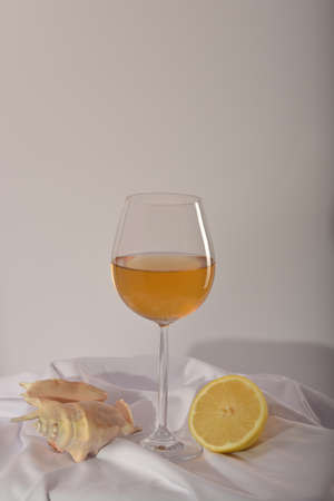 still life. beautiful glass with white wine, sea clam shell and lemon on a light background.の写真素材