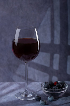 still life. Large beautiful glass with red wine, plate with blue berries on a dark background with creative lightingの写真素材