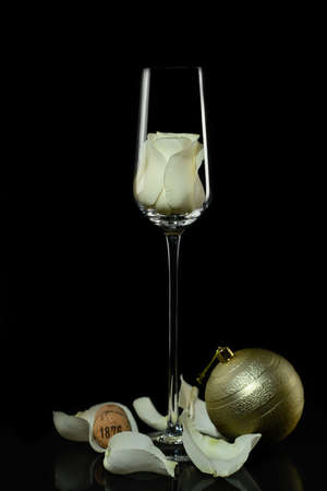 Still life. Elegant glass of thin glass for champagne with a rose inside, scattered rose petals and a large Christmas tree toy on a dark backgroundの写真素材