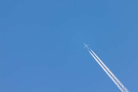 Flying plane leaves an inversion trail in the airの写真素材